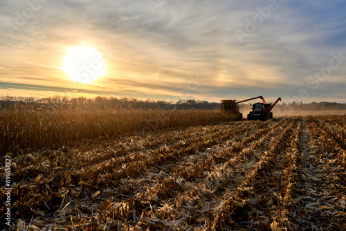 Combine harvesting corn crop offloading to a tag-along tractor and trailer.