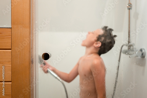 Boy holding hand shower while taking bath in bathroom photo