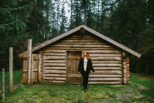 Woman standing by a rustic log cabin in the woods photo