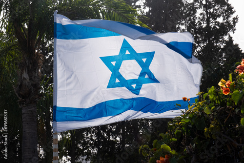 Independence day  (Yom Haatzmaut) in israel. Hanging official flag waving on wind with Star of David on it against trees. photo