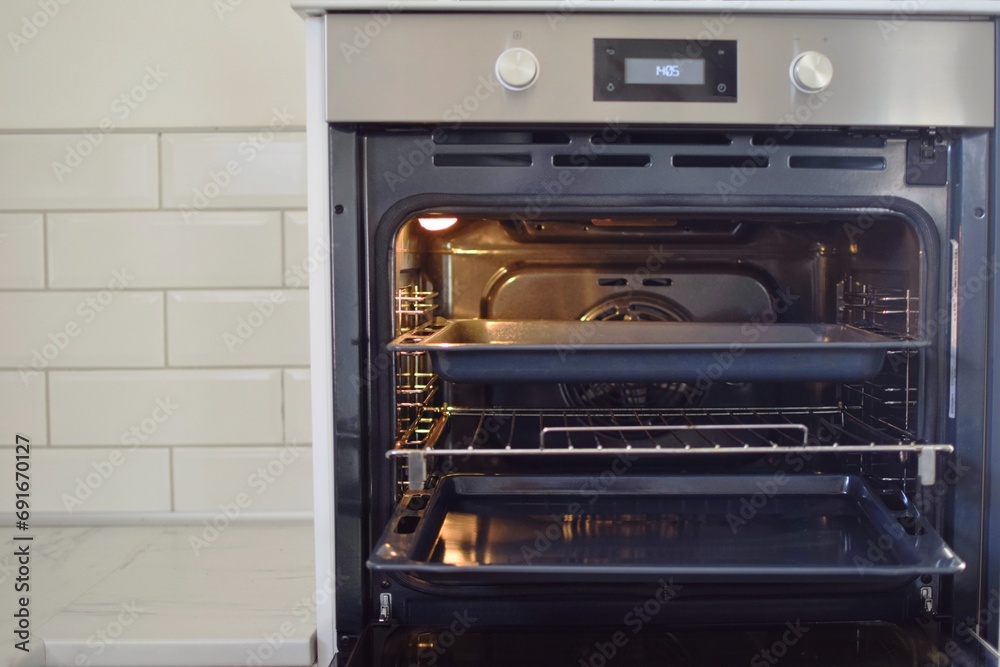 The oven door is open. The light is on inside and the oven tray are visible. The oven door is open. The light is on inside and the oven tray are visible.