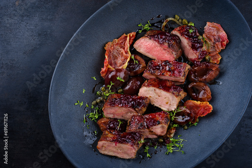 Traditional fried wild hare back filet with plums, cranberries and bacon in red wine jus served as top view on Nordic design plate with copy space