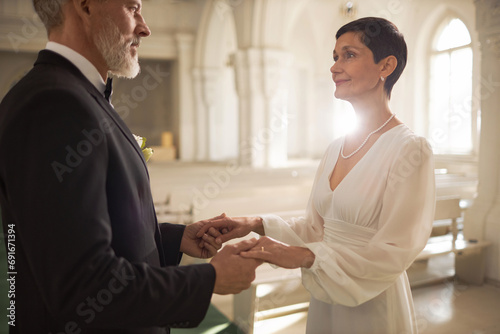 Waist up portrait of senior couple holding hands and exchanging wedding vows in church