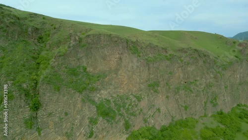 An aerial view of high rocky mountains covered with green grass and trees on an overcast summer day. Small villages near the river with country roads. Dzoraget River, Canyon, Armenia. Drone footage