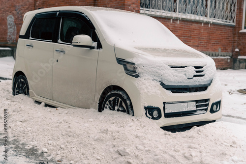 Fototapeta Naklejka Na Ścianę i Meble -  A small car parked on a winter city street is littered with dirty snow from snow removal equipment
