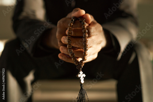 Closeup of priest holding wooden rosary beads and praying in ethereal sunlight, copy space photo