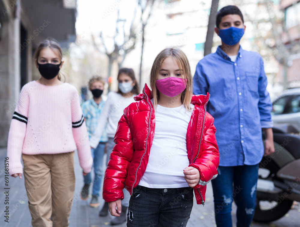 Focused preteen girl in pink protective mask walking along city street on spring day. New life reality during coronavirus pandemic