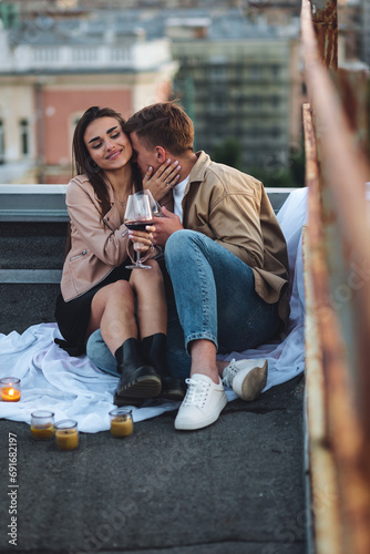Romantic beautiful surprise on Saint Valentine's Day for a girlfriend. Loving young couple having dinner on a rooftop on sunset evening with candles, wine. Skyscrapers on background, urban cityscape