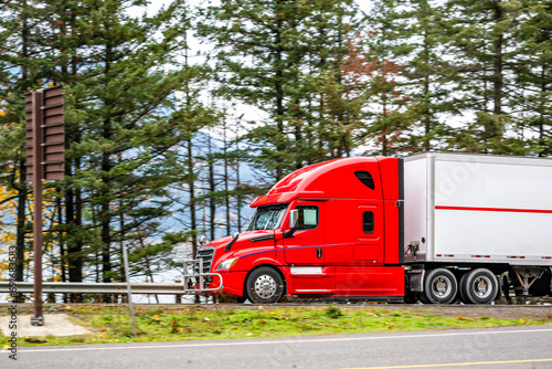 Fire red big rig semi truck transporting cargo in dry van semi trailer running on the road along the Columbia river