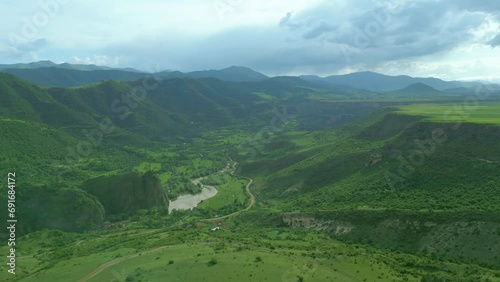An aerial view of high rocky mountains covered with green grass and trees on an overcast summer day. Small villages near the river with country roads. Dzoraget River, Canyon, Armenia. Drone footage photo