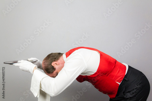 Portrait of a Waiter or Servant in Red Vest Bowing Profusely and Offering Silver Tray. Act of Sycophantic Servitude.