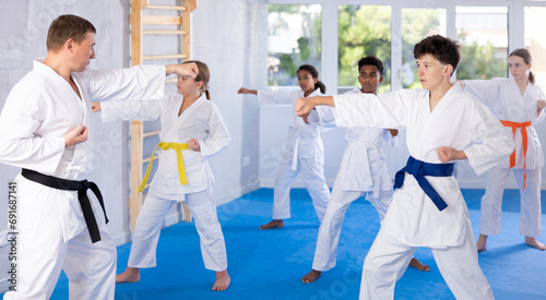 Motivated tween boy in kimono standing in attacking stance, practicing punches or hand striking techniques as part of kata with group of teenagers