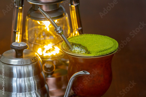 Traditional chimarrão prepared with yerba mate (Ilex paraguariesis) in a porongo gourd, next to a vintage lamp and barista-style gooseneck kettle photo