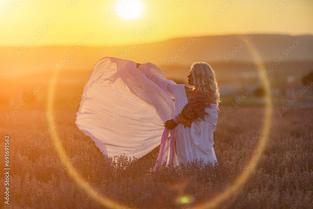 Blonde woman poses in lavender field at sunset. Happy woman in white dress holds lavender bouquet. Aromatherapy concept, lavender oil, photo session in lavender - obrazy, fototapety, plakaty 