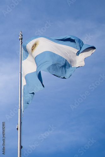 Bandera argentina flameando en mastil, delante de un cielo azul