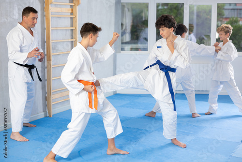 Sportive children wearing kimono working in pair mastering new karate moves during group class in gym