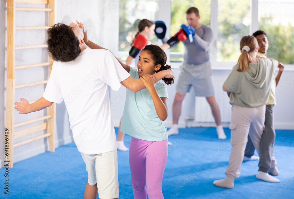 Girls and boys practicing in pair self-defence movements with male trainer supervision