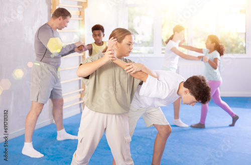 Tweens attending self-defense classes under careful supervision of instructor at training center. Focused girl applying armlock technique in sparring with boy