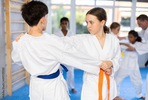 Determined motivated teenage girl working on martial arts skills in pair with boy during group training ..