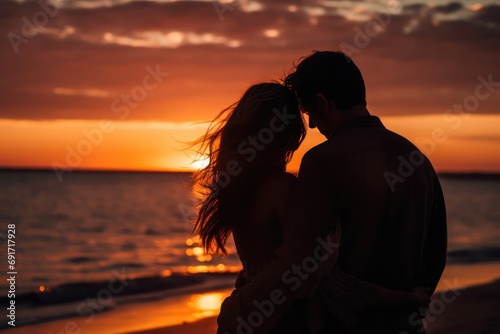 A man and a woman hugging and looking at the sunset on the beach  photo