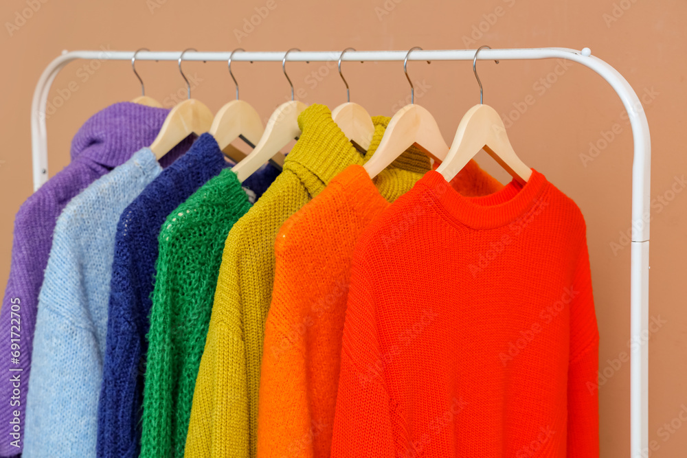 Hangers with colorful clothes hanging on rack near color wall, closeup