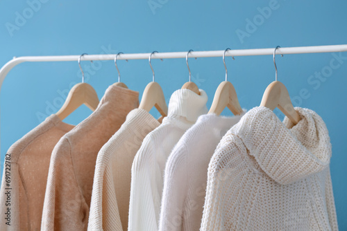Rack with stylish female sweaters on color background, closeup