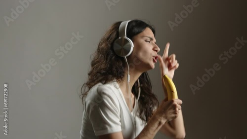 A happy girl in headphones dances and sings into an imaginary banana microphone. She is very happy and joyful. High quality 4k footage photo