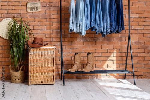 Rack with stylish female jeans, shoes and houseplant near brick wall in boutique