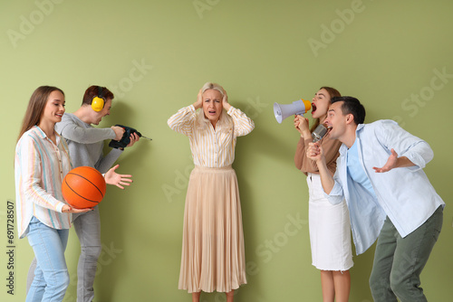 Mature woman suffering from noisy neighbours on green background