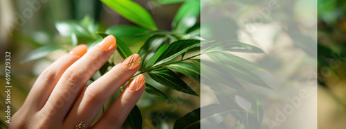 A hand gracefully touches green leaves, the nails matching the Peach Fuzz 2024 color, symbolizing a connection with nature.