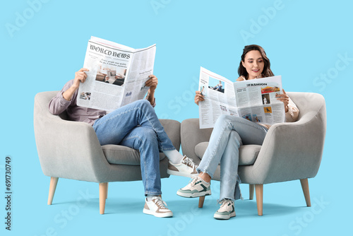 Young couple reading newspapers in armchairs on blue background photo