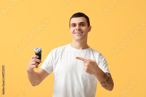 Handsome young man pointing at electric shaver on yellow background