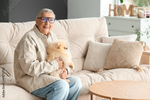 Senior woman in eyeglasses with Pomeranian dog sitting on sofa at home