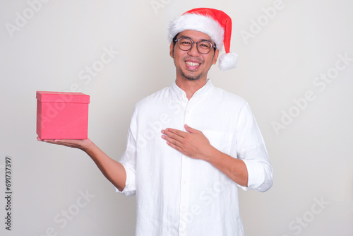 A man wearing christmas hat showing grateful gesture while holding a gift box photo