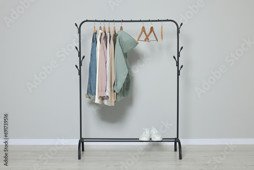 Rack with stylish clothes on wooden hangers and shoes near light grey wall photo