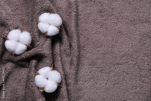 Fluffy cotton flowers on brown terry towel, top view. Space for text