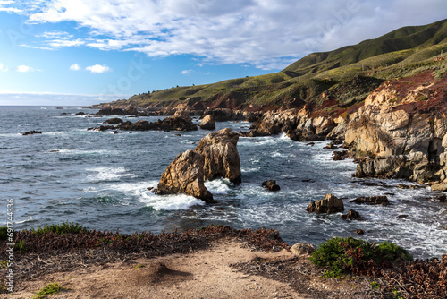 Rocky coastline of Garrapata Beach, south of Monterey, California. Giant rocks just offshore. Waves washing against rocky cliff face. 
 photo
