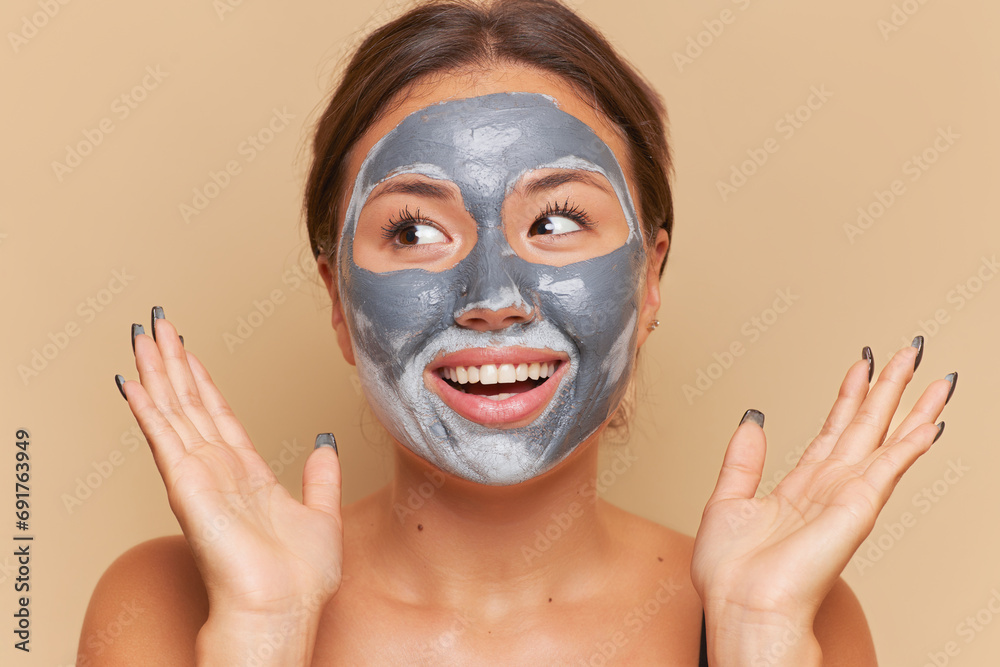 Close up portrait of smiling woman doing facial mask with clay over studio background, skincare concept, copy space Close up portrait of smiling woman doing facial mask with clay over studio background, skincare concept, copy space
