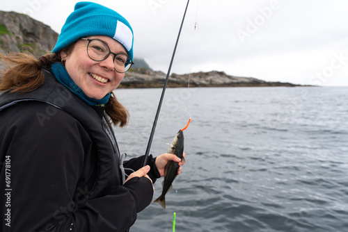 A smiling female fisherman proudly displays a large catch while standing on a boat in the Norwegian Sea, enjoying her hobby and the beauty of the ocean on a sunny day.