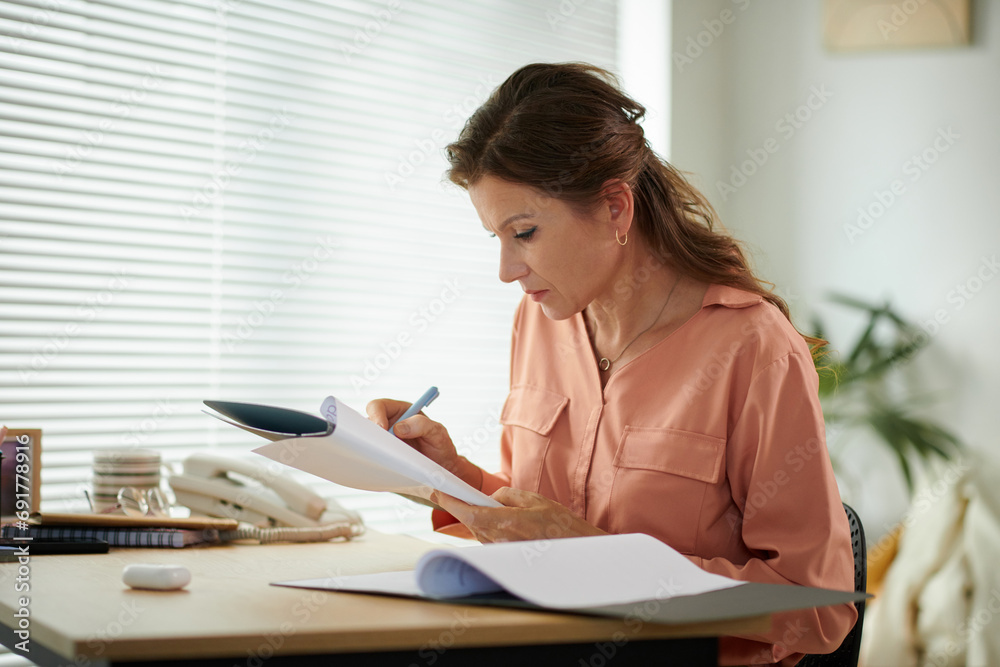 Serious mature businesswoman correcting data in report when working in office Serious mature businesswoman correcting data in report when working in office