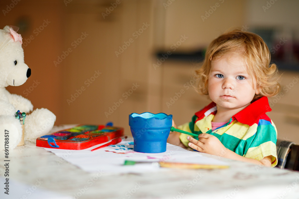 Cute adorable baby girl learning painting with water colors. Little toddler child drawing at home, using colorful brushes. Healthy happy daughter experimenting with colors, water at home or nursery. Cute adorable baby girl learning painting with water colors. Little toddler child drawing at home, using colorful brushes. Healthy happy daughter experimenting with colors, water at home or nursery.