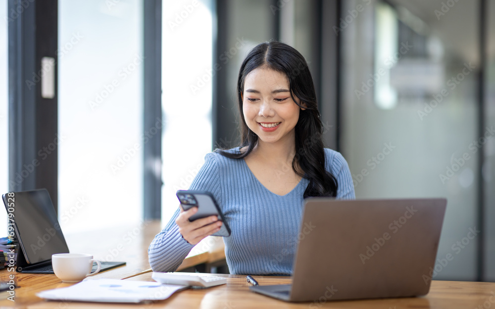 Portrait of Asian young female working on laptop with phone at the office