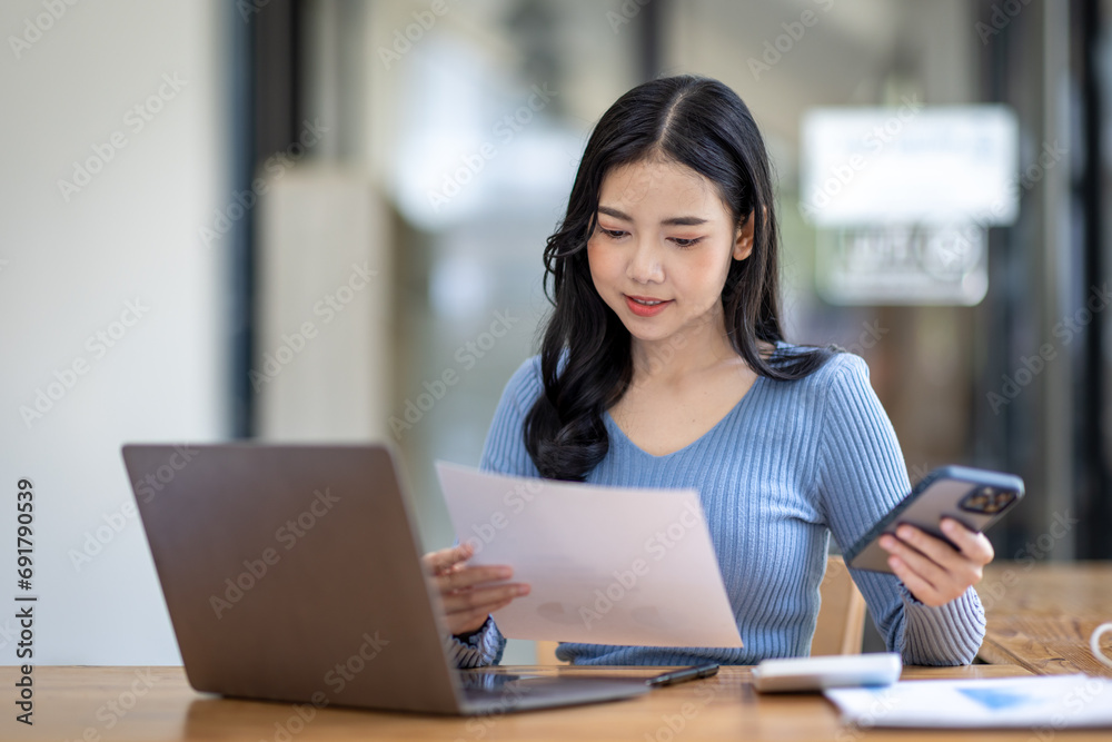 Portrait of Asian young female working on laptop with phone at the office Portrait of Asian young female working on laptop with phone at the office
