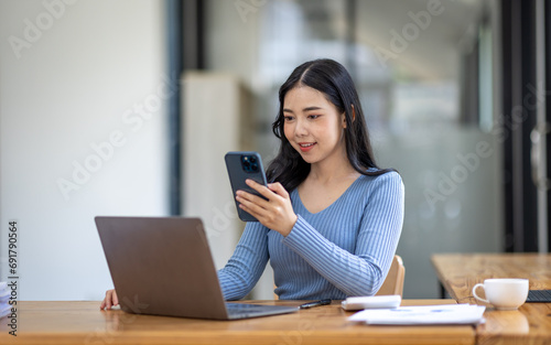 Portrait of Asian young female working on laptop with phone at the office