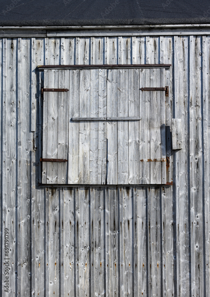 Weathered wooden siding with a closed window shutter, as a rustic background
Weathered wooden siding with a closed window shutter, as a rustic background