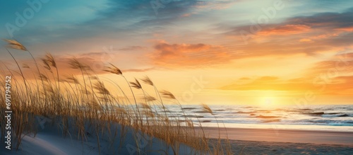 Sunset over sand dune, grass, beach, sea, sky, clouds.