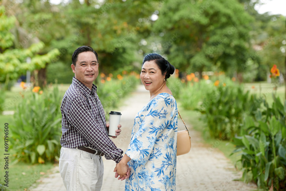 Elderly couple holding hands and walking back to camera when walking in park Elderly couple holding hands and walking back to camera when walking in park