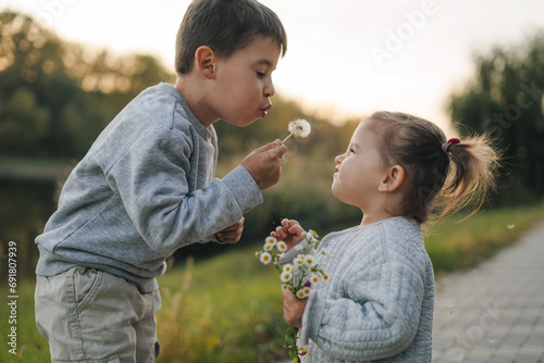 School kid boy and little baby girl blowing on a dandelion flowers on the nature in the summer. Having fun. Family of two love, together photo