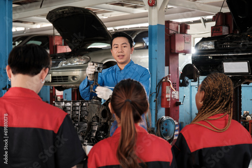 Specialist lecture, a male supervisor engineer train and describe automotive engines with mechanic worker staff teams for repair work at car service garage and maintenance jobs in automobile industry.