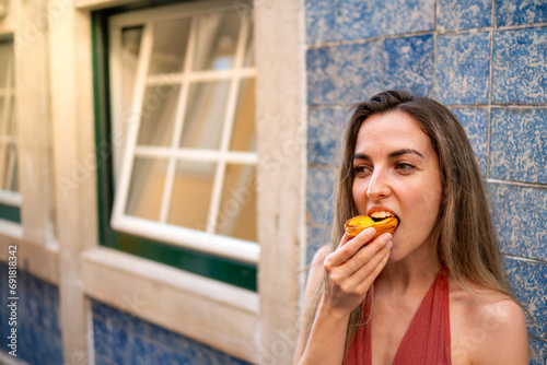 Close-Up, Frontal View of young Woman Enjoying a Traditional Portuguese Pastel de Nata, Captured Horizontally in Daylight
